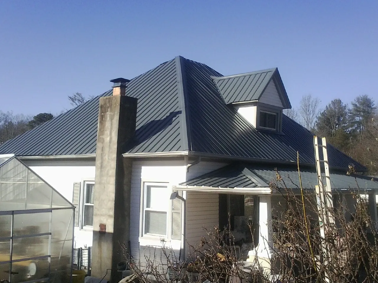 Dark blue standing seam metal roof on a white farmhouse with dormer — Slate & Tile Roof Repair by Roofing Brothers in Saukville