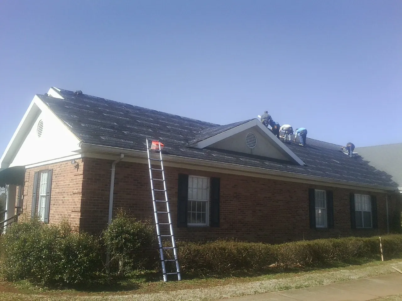 Crew tearing shingles off a brick ranch roof with a ladder set — Emergency Roof Repair work by our crew in Saukville