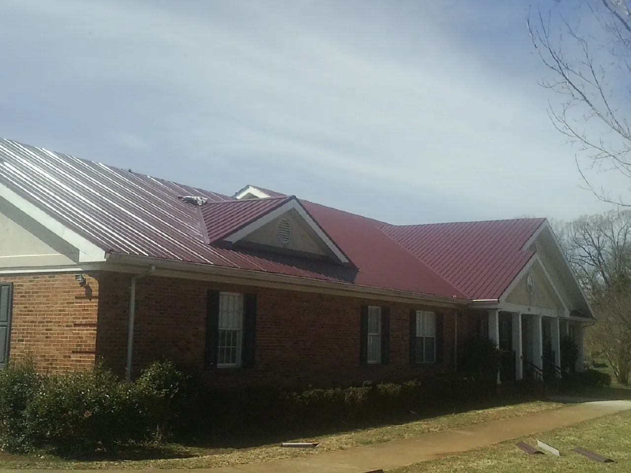 Red metal roof with gabled entries on a long brick building, from a Hail Damage Roof Repair job in Saukville