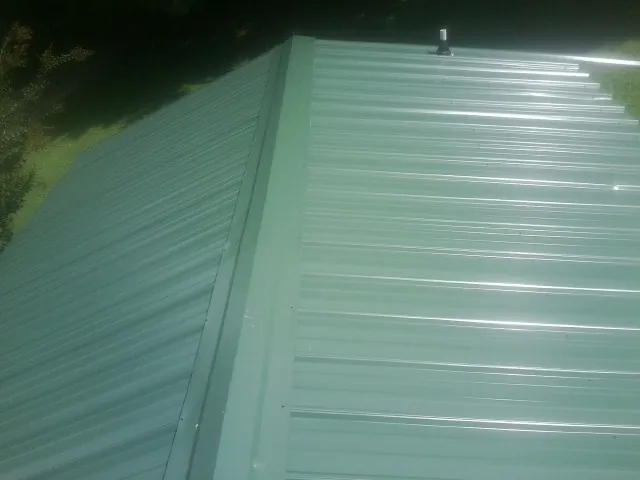 New green metal panels meeting at the ridge of a roof — Flat Roof Repair work by our crew in Saukville