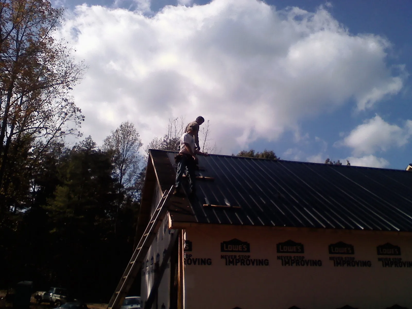 Roofer fastening dark metal panels high against a cloudy sky, from a Roof Inspection job in Saukville