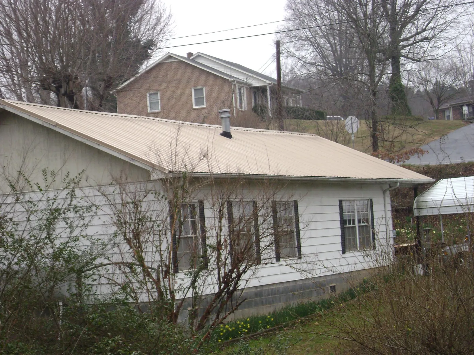 Tan metal roof on a white sided house set into a hillside — Commercial Roofing by Roofing Brothers in Saukville